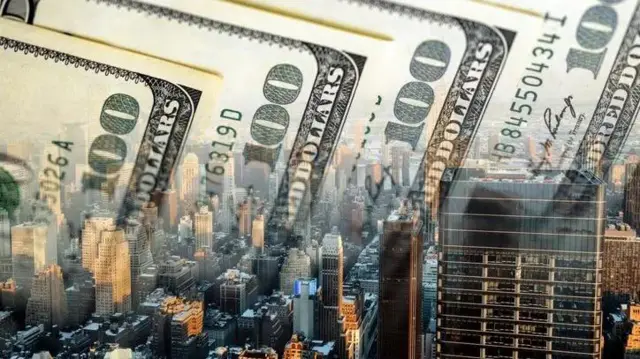 ඩොලර් නෝට්ටු කිහිපයක් සහ නගරයක ගොඩනැගිලි දිස්වන ඡායාරූපයක්.