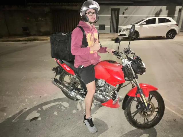 O criador de conteúdo Henrique Batista em cima de uma moto, com capacete e mochila