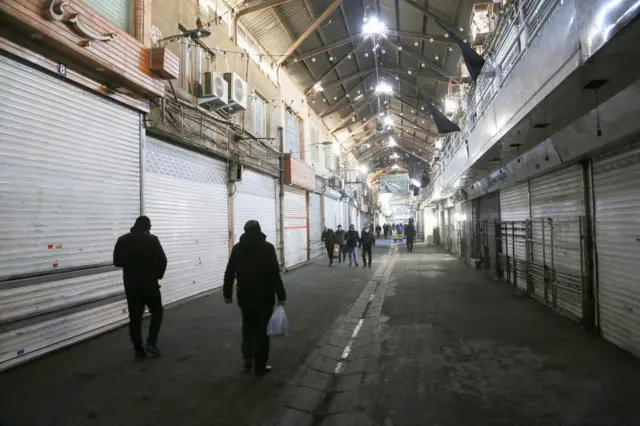 أناس يسيرون بجانب محال تجارية مغلقة في طهران احتجاجاً على غلاء المعيشة وانخفاض قمية العملة المحلية مقابل العملات الأجنبية