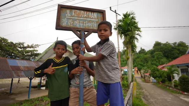Anak-anak dari Kampung Karya Baru berpose di palang Jalan Kebudayaan yang ditulis dalam aksara Hangeul.