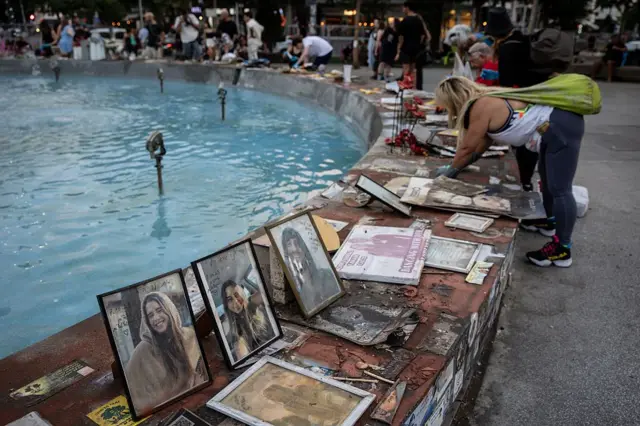 Bir havuzu çeşmenin çevresinde çok sayıda rehine fotoğrafı var, bir kadın ortalığı düzeltiyor