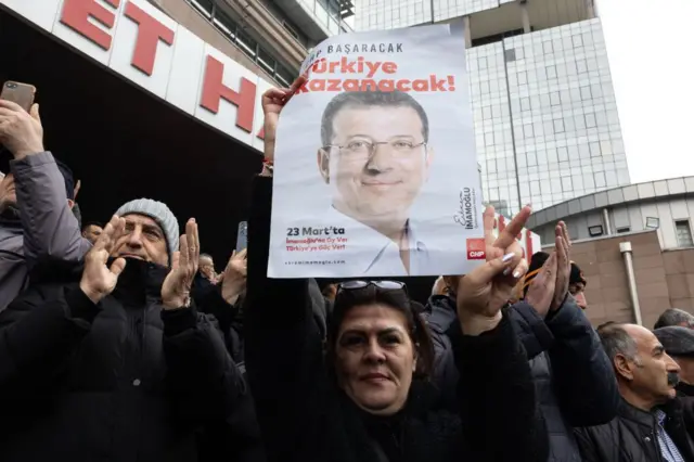 Bir kadın CHP binası önünde Ekrem İmamoğlu posteri tutuyor.