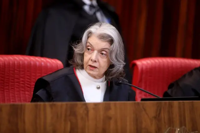 Cármen Lúcia com feição séria fala sentada em uma cadeira vermelha no plenário do TSE