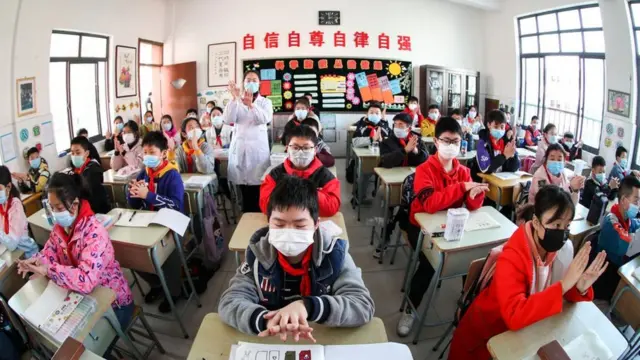 Alumnos asiáticos con tapabocas y limpiándose las manos.