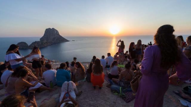 Turistas sentados mirando una puesta de sol.