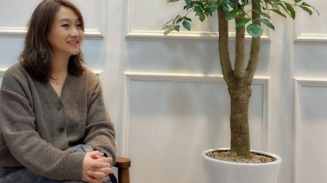 Julia Yoon sits on a chair next to a plant.