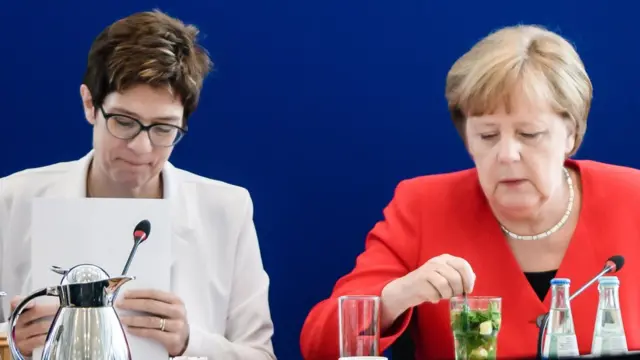Annegret Kramp-Karrenbauer e Angela Merkel sentadas à mesa durante evento