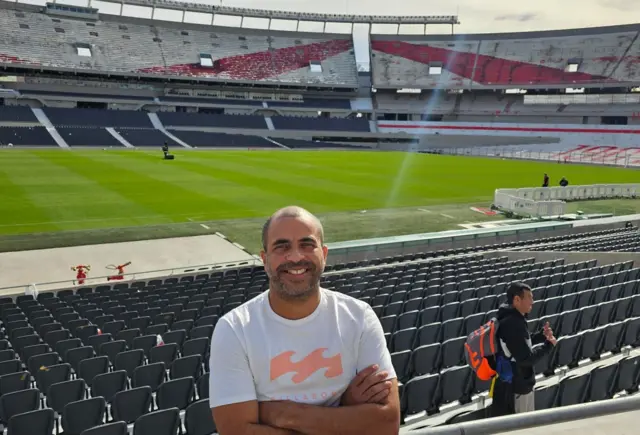 Homem brasileiro de pele clara, barba e calvo em um estádio de futebol