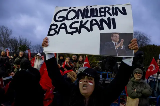 19 mart'ın yıldönümündeki protestoya katılan bir kadın elinde "Gönüllerin başkanı" yazan ve üzerinde ekrem imamoğlu'nun fotoğrafının olduğu bir pankart tutuyor.