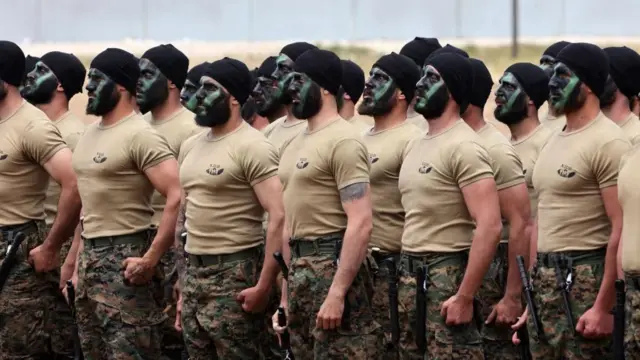 Members of Hezbollah with their faces painted in cammo stand in a line