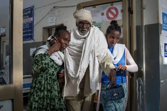 ሁለት ሴቶች አዛውንትን ግራ እና ቀኝ ደግፈው እዘው