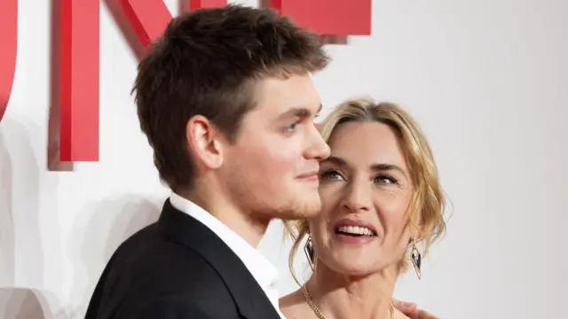 Joe Anders na czerwonym dywanie ze swoją mamą Kate Winslet. Winslet patrzy na niego z dumą i uśmiechem.
