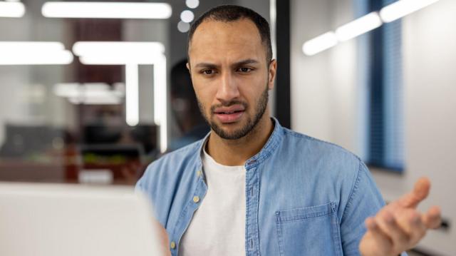 Man in denim shirt looks confused during video interview over laptop