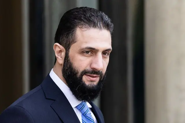 رئيس السلطة الانتقالية في سوريا،أحمد الشرع، مرتدياً سترة زرقاء قميصاً أبيض وربطة عنق بها درجات من اللون الأزرق.