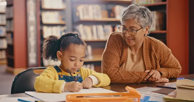 Une femme senior noire africaine avec enfant apprenant dans une bibliothèque scolaire.