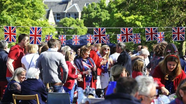 Revellers sit under decorations with Britain's Union flags during a street party to celebrate the Queen's Diamond Jubilee in Edinburgh on June 3, 2012