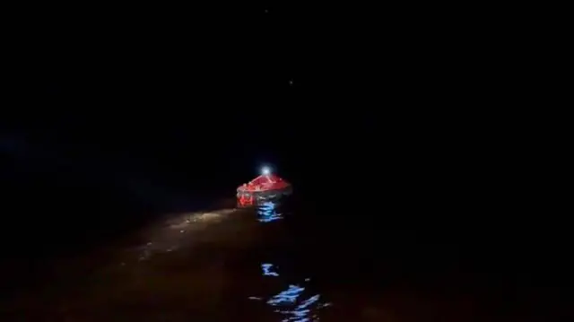 暗闇の中、海に浮かぶ赤いゴム製の救命ボートの写真。ボートの上部で照明が輝いているのが見える