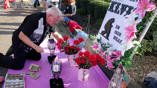 روجر إنلباي من ولاية ميسوري الأمريكية يؤسس نصبا لإلفيس خارج بوابات غريسلاند أثناء انتظاره بدء تجمع لإضاءة الشموع أحياء لذكرى إلفيس بريسلي الأربعين.