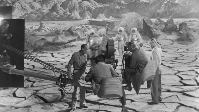 1950: Actors wearing spacesuits walk on a replica of the lunar surface, as director Irving Pichel and a cinematographer sit on a camera crane, preparing to shoot a scene on the set of Pichel's film, 'Destination Moon.' There is a painted celestial backdrop with mountains on the horizon. (Photo by Hulton Archive/Getty Images)