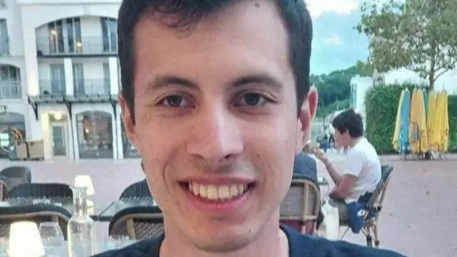 Primer plano de Quentin Deranque, detrás se ven unas mesas en una terraza y una persona tomando algo.