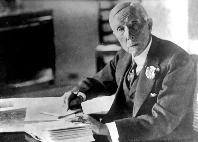 John D. Rockefeller, posa escribiendo documentos en un escritorio. 