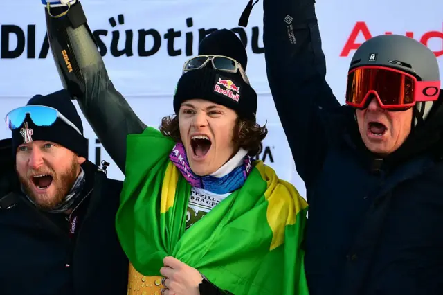 O brasileiro Lucas Pinheiro Braathen (C), segundo colocado, comemora com sua equipe no pódio após competir no slalom gigante masculino da Copa do Mundo de Esqui Alpino da FIS 2025-2026, em Alta Badia, norte da Itália, em 21 de dezembro de 2025.