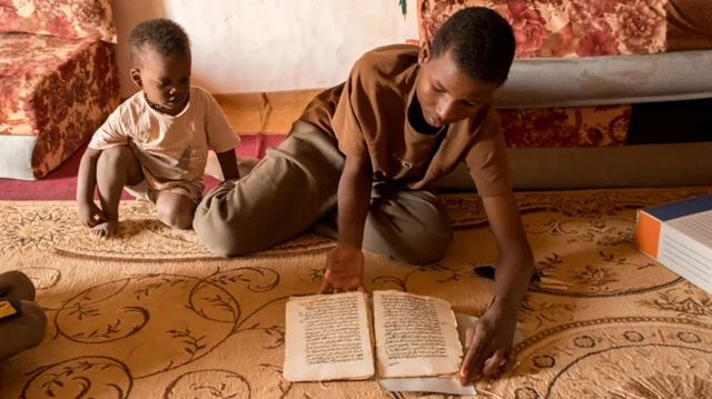 Un jeune homme lisant un document écris en arabe, à côté d'un enfant qui observe.