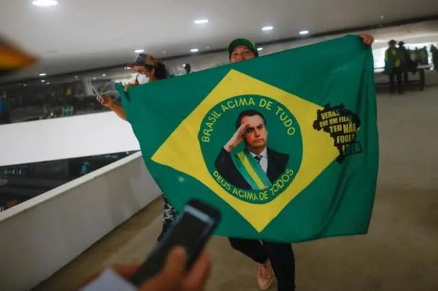Una mujer que participó en el asalto a las sedes de los poderes en Brasil muestra una bandera con el rostro de Bolsonaro.