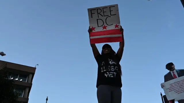 Протест в Вашингтоне: человек держит над головой плакат "Свободу округу Колумбия"