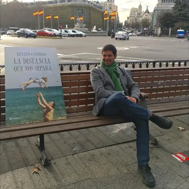 Renato Cisneros con la portada de su libro "La distancia que nos separa" ante la Cibeles en Madrid.