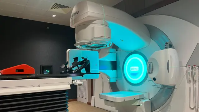 Imashini ya 'radiotherapy' iri mu bitaro, icanyemo urumuri rw'ubururu. Hari igitanda abarwayi baryamaho, n'ahantu ho kurambika umutwe. 