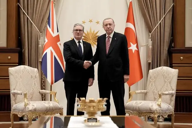 İki erkek el sıkışıyor. Arkalarında Birleşik Krallık ve Türkiye bayrakları var 