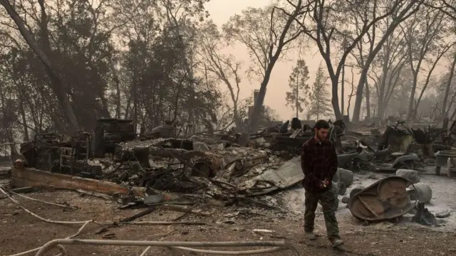 Un joven camina por los restos de su casa, ahora en cenizas