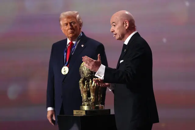 Дональд Трамп и Джанни Инфантино в темных костюмах на церемонии вручения президенту США премии мира ФИФА - позолоченный кубок, в его основе руки, держащие земной шар 