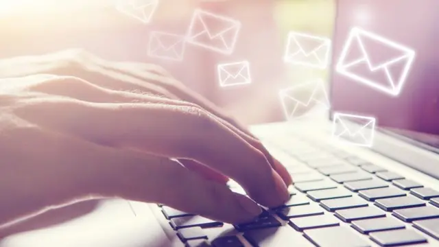 Una persona escribiendo en un teclado. Símbolos de "correo" flotan encima