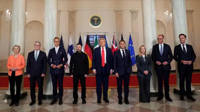 Во время встречи в Белом доме: девять лидеров стоят на фоне флагов своих стран. В центре - президент Зеленский и Дональд Трамп