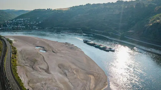 Vista aérea de un buque de carga pasando junto a un enorme banco de arena en el río Rin.