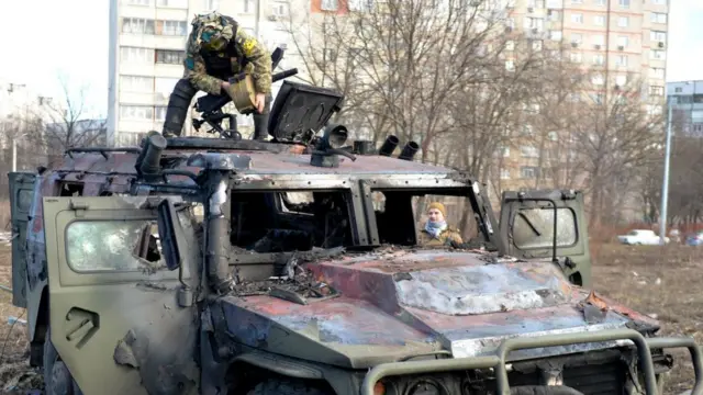 A Ukrainian Territorial Defence fighter examines a destroyed Russian infantry vehicle in Kharkiv, Ukraine