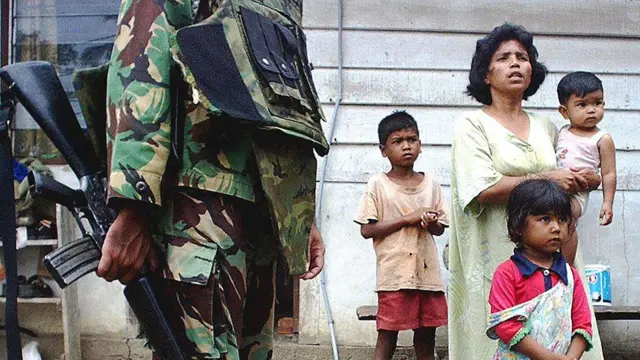 Seorang perempuan Aceh dan anak-anaknya menyaksikan seorang tentara memeriksa identitas penduduk setelah baku tembak antara militer Indonesia dan GAM di Aceh Besar, pada 16 Agustus 2003.