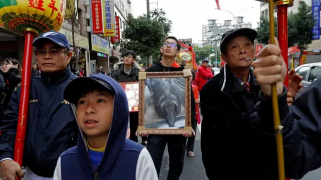 Một thành viên trong gia đình chủ nhân con heo thắng cuộc cầm ảnh của con heo này tại lễ diễu hành tại quận Sanxia, ở Tân Đài Bắc, Đài Loan, 0/02/2017.