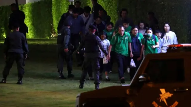 عدد من الناس في أثناء خروجهم من مركز التسوق برفقة أفراد من الشرطة التايلاندية.