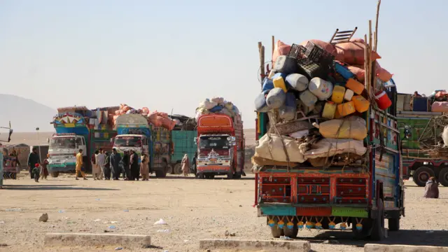 تصویر لاریهای حامل افغانها با لوازم خانهشان. شماری از مهاجران به شمول زنان، کودکان و مردان در مقابل لاریها ایستادهاند.