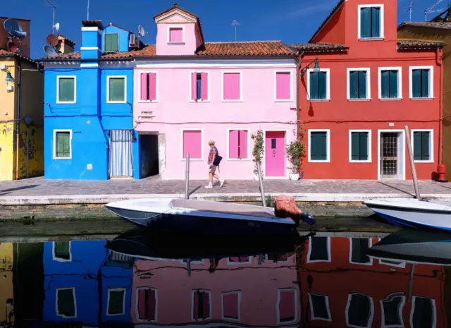 Um homem caminha na frente21 cassinoum conjunto21 cassinocasas pintadas, ao longo21 cassinoum canal21 cassinoágua, refletidas21 cassinouma poça d'água