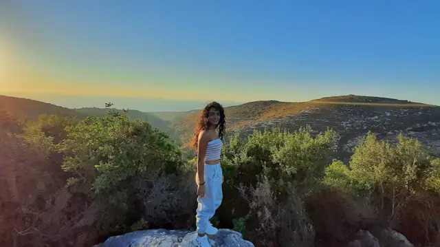 Maria Shaya parada sobre una roca con vistas a un hermoso valle en agosto de 2020