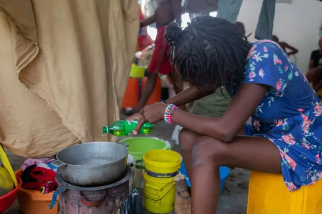 Une jeune femme cuisine dans une pièce d'un camp de réfugiés à Port-au-Prince.