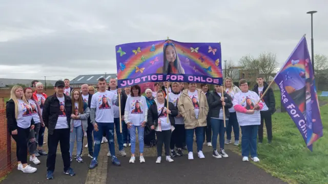 Un grupo de familiares y amigos con camisetas y pancartas de "Justicia para Chloe". Están en un parque.