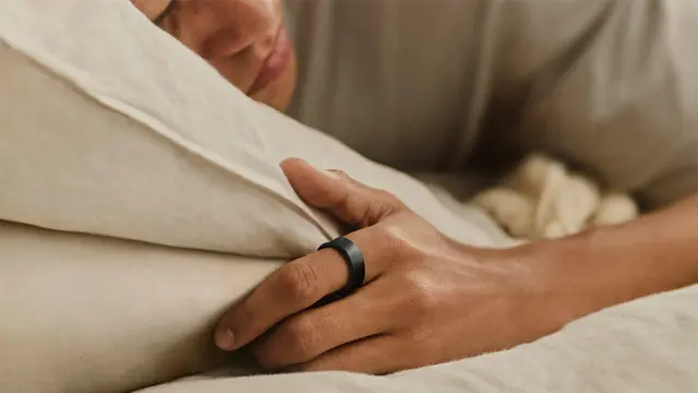 La imagen para prensa muestra a una mujer acostada con la cabeza sobre una almohada y los ojos cerrados mientras usa el Galaxy Ring de Samsung.