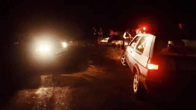Automobili sa upaljenim farovima tokom noći na blokadi puta