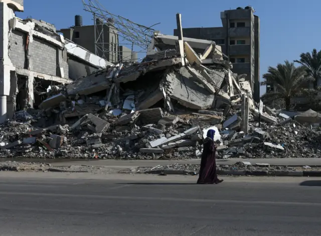 Mulher anda em meio a escombros em Gaza 