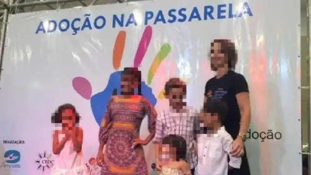 Crianças e uma mulher adulta posambubble shooter grátis para jogarfrente a painel com os dizeres: Adoção na passarela